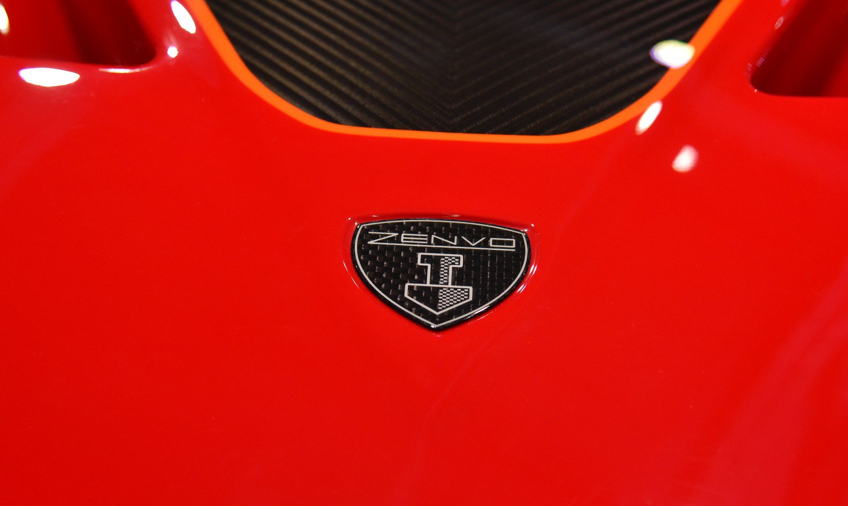 Close-up of Zenvo badge on red hood with carbon fiber inset