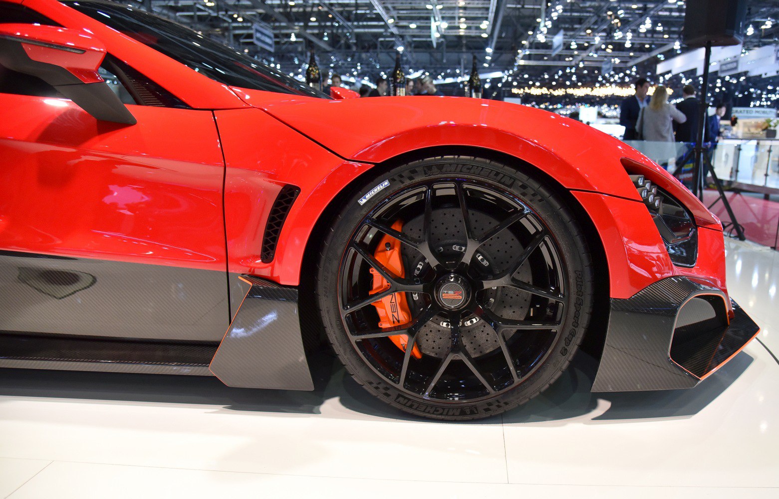 Front wheel with black rim, orange brake caliper, and carbon fiber aerodynamic parts