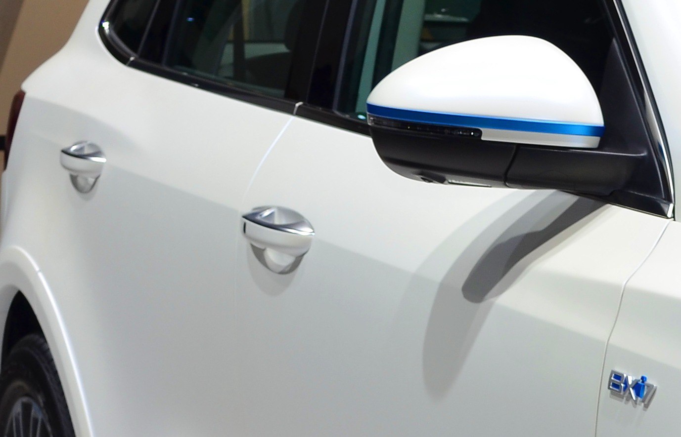 Close-up of side mirror with blue trim and door handles on a white vehicle.