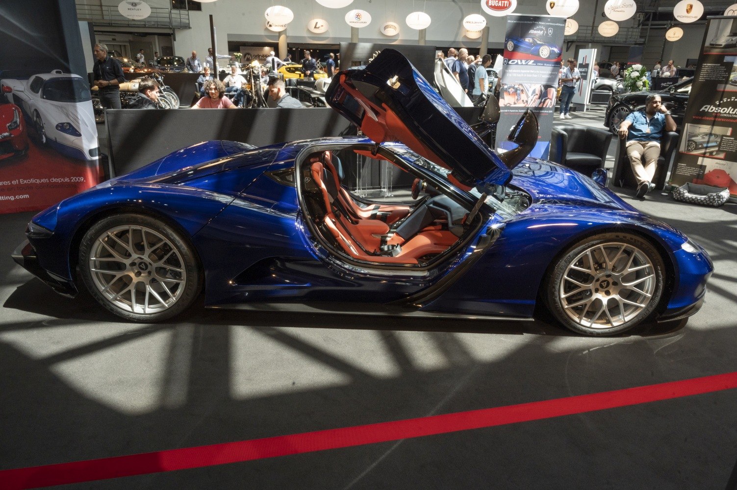 Side profile of blue hypercar with open scissor doors and red interior seats