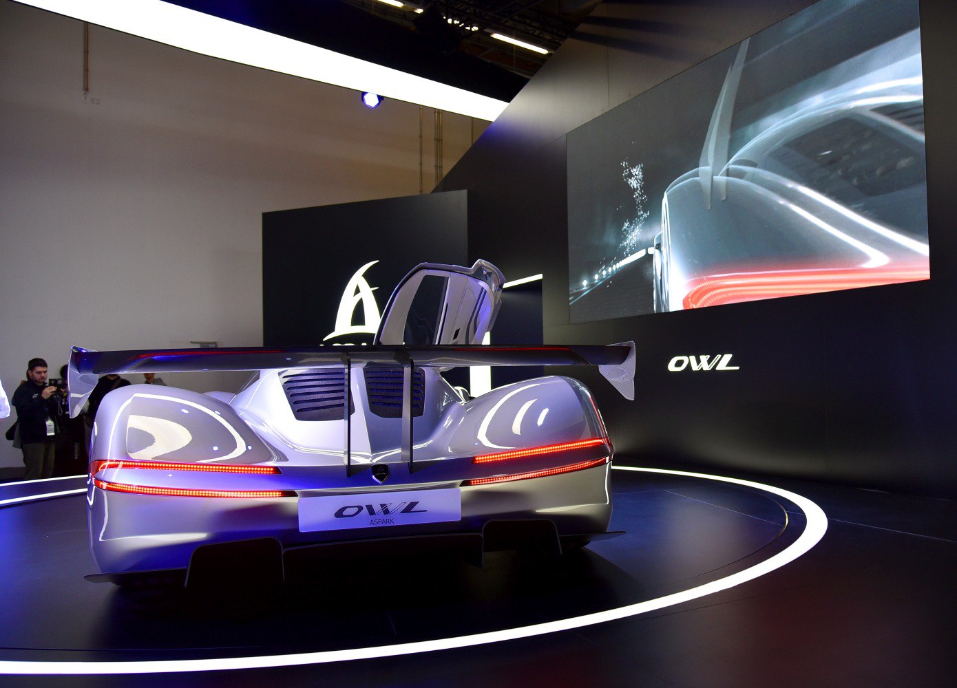 Rear view of a sleek car with a large rear wing and one gull-wing door open