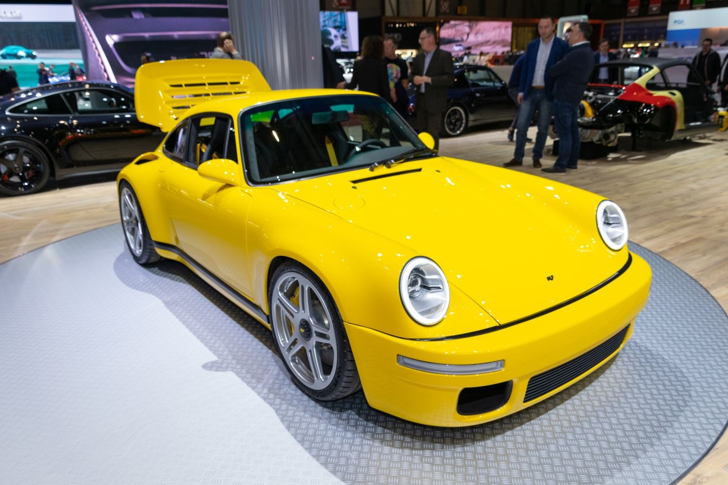 Bright yellow sports car with open rear engine hood on display.