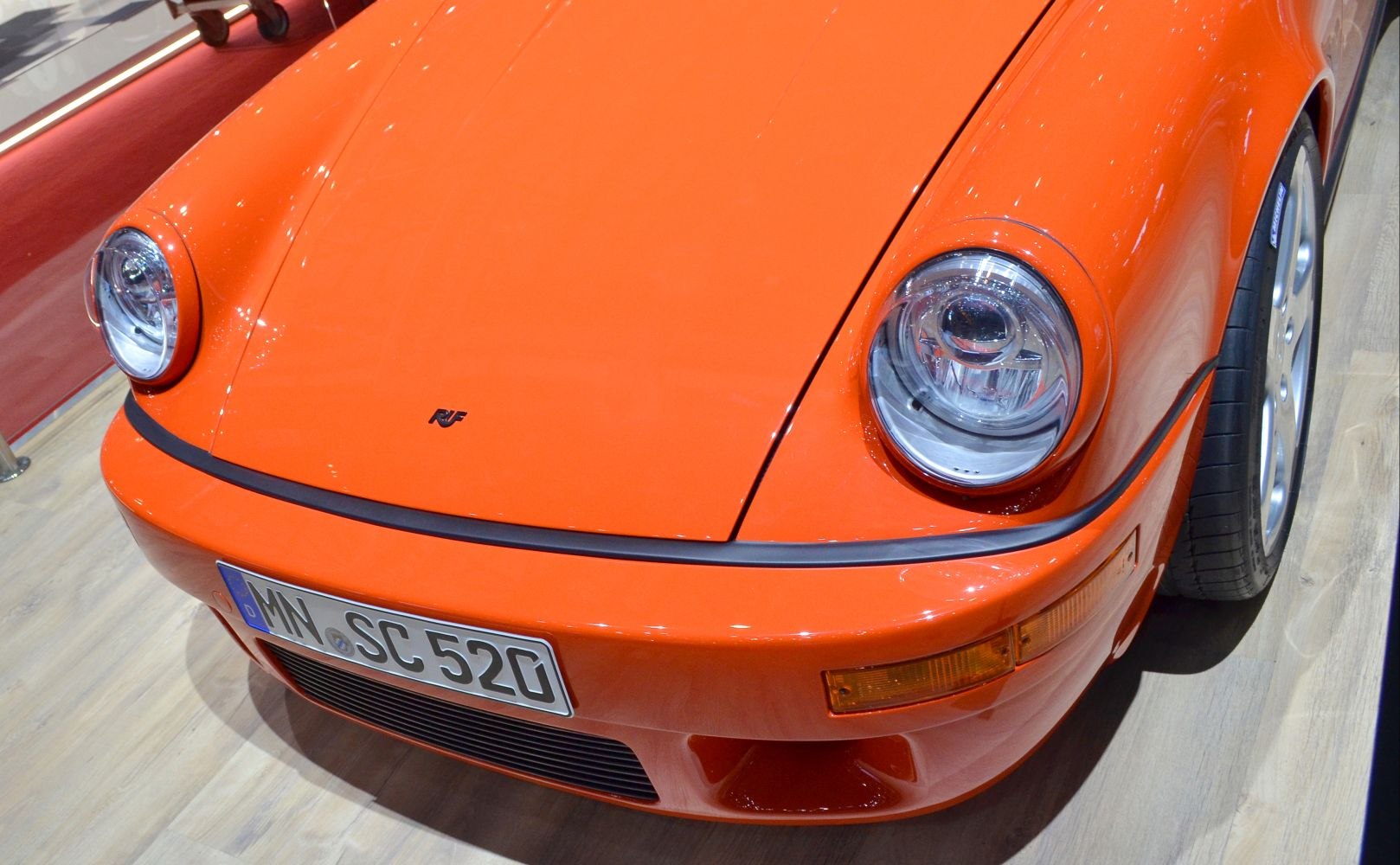 Close-up of front headlight, hood, bumper in bright orange.