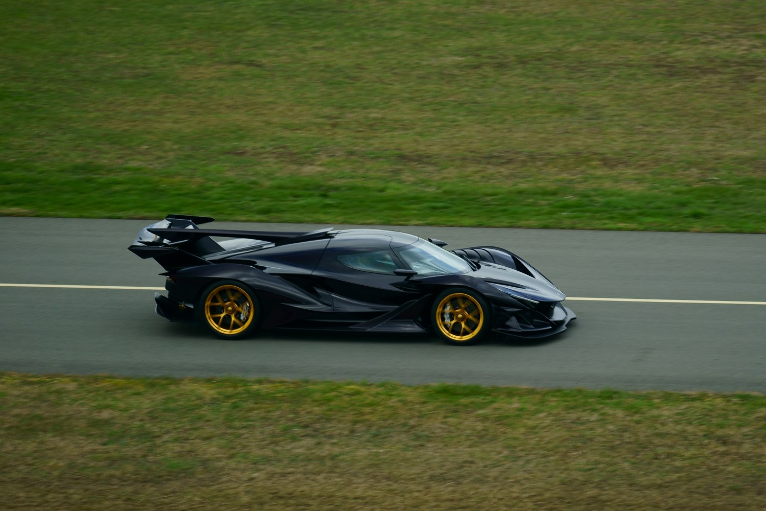 Black hypercar with aerodynamic wing and gold wheels on track
