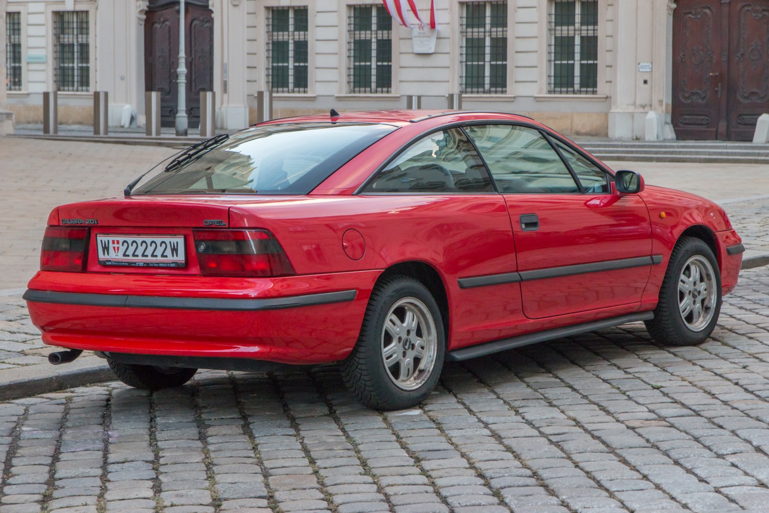 Red 1990s sports coupe rear side view with taillights and five-spoke wheels