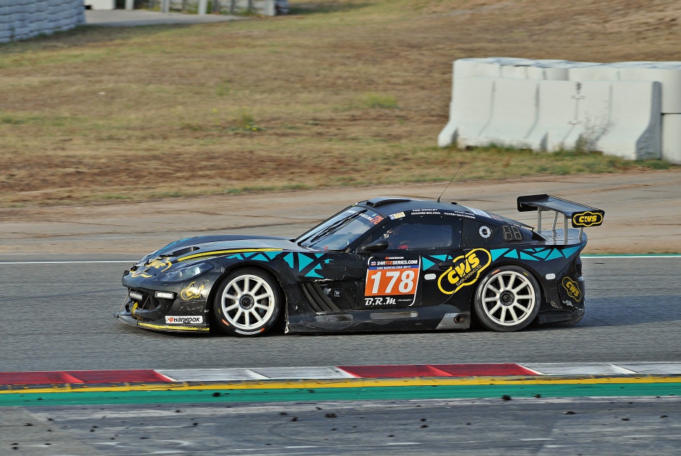 Side view of a racing car with aerodynamic body, racing decals, and large rear wing.