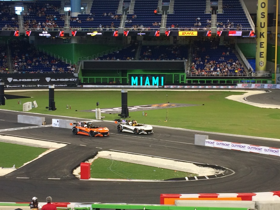 Two lightweight open cockpit sports cars racing on a tight stadium track corner.