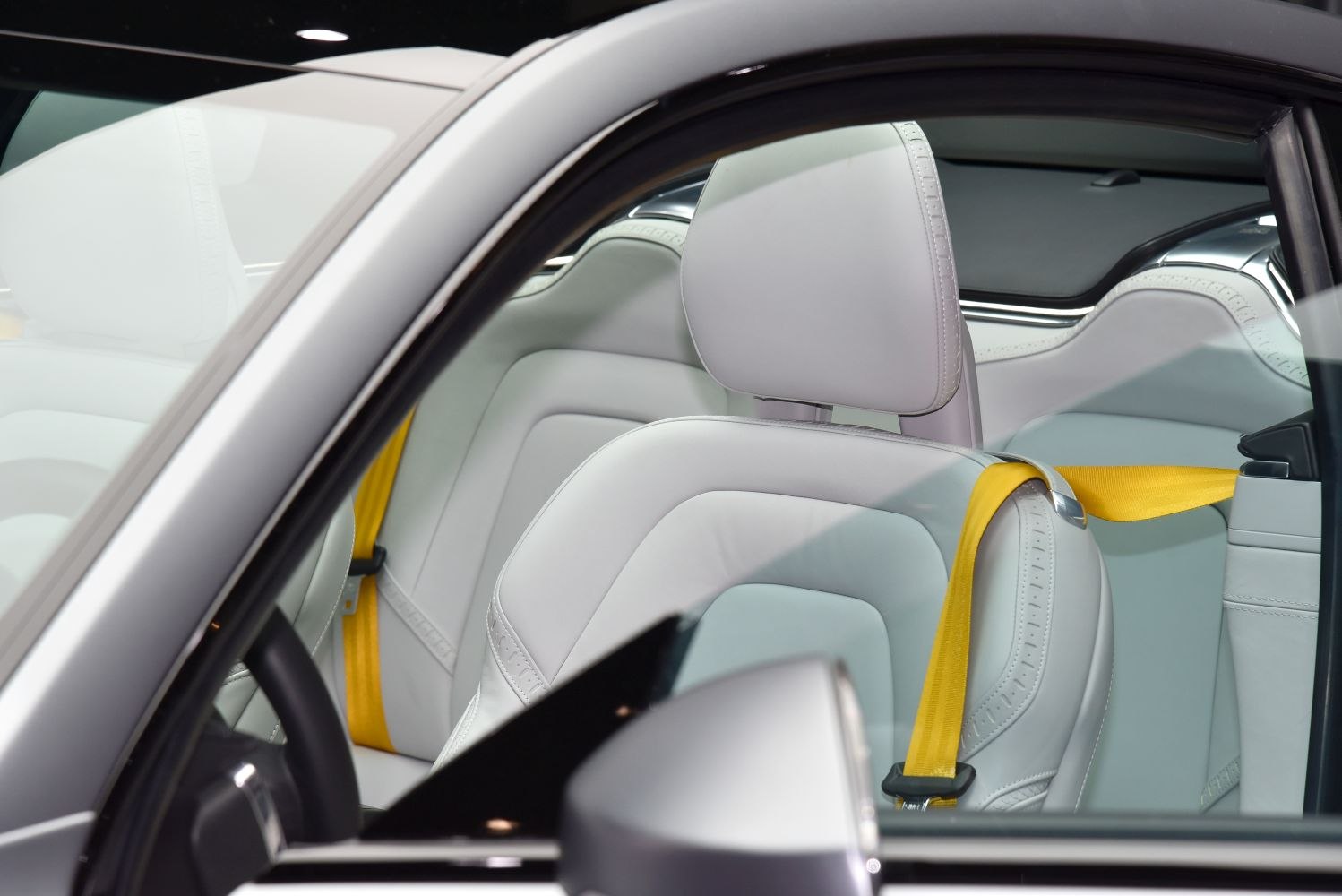 White leather seats with yellow seat belts inside a car.