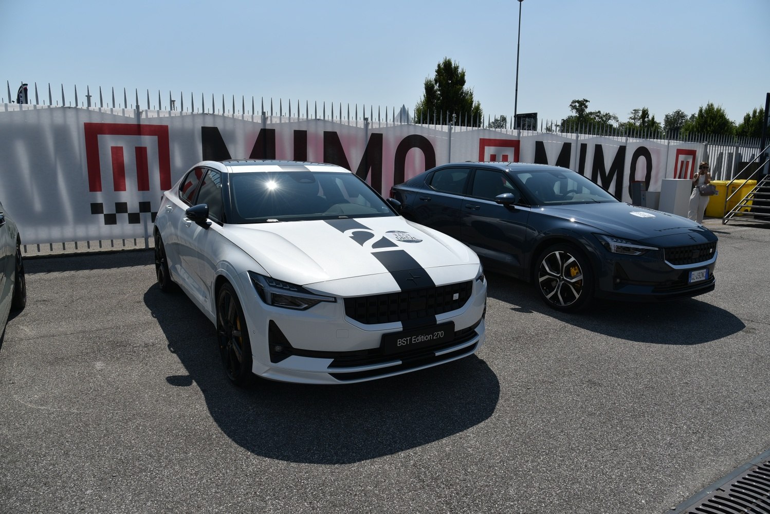 Two Polestar 2 electric sedans parked side by side, one white with racing stripes, one dark-colored.