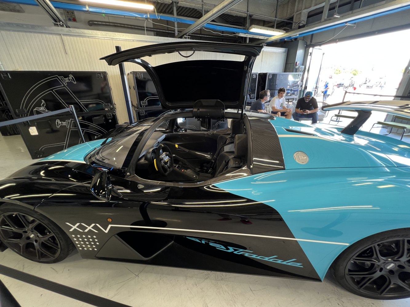 Side view of a sports car with gullwing door open and two-tone black and blue body