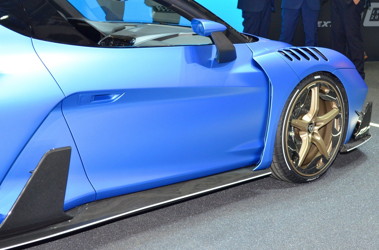 Close-up on side door, aerodynamic fins, carbon fiber splitter, and bronze alloy front wheel
