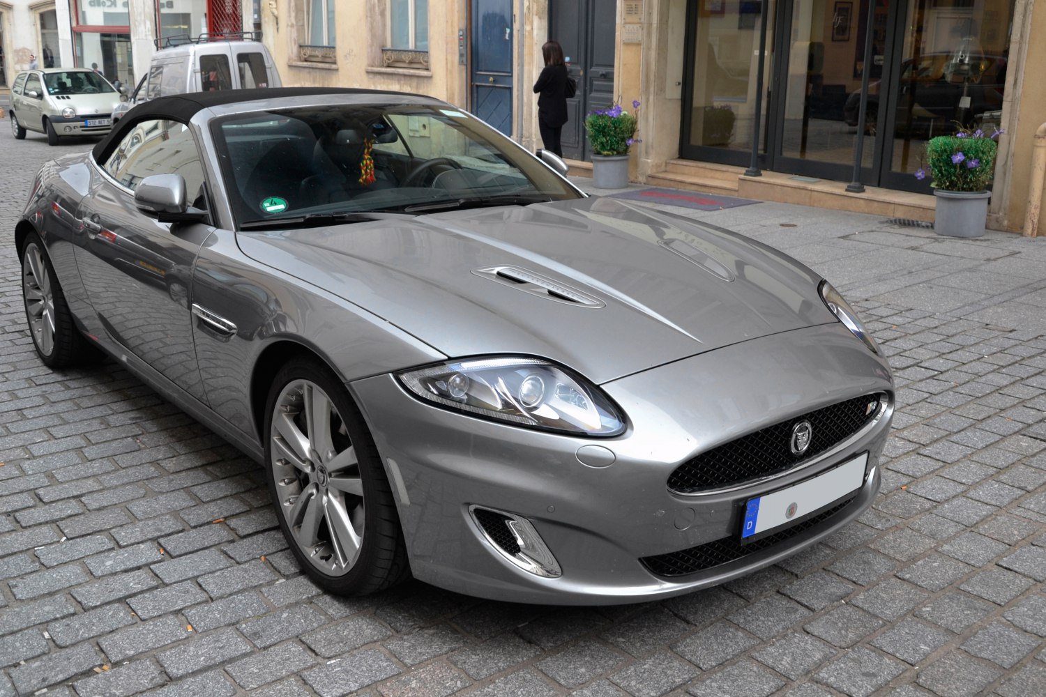Silver convertible with distinct headlights and hood vents, black soft top roof