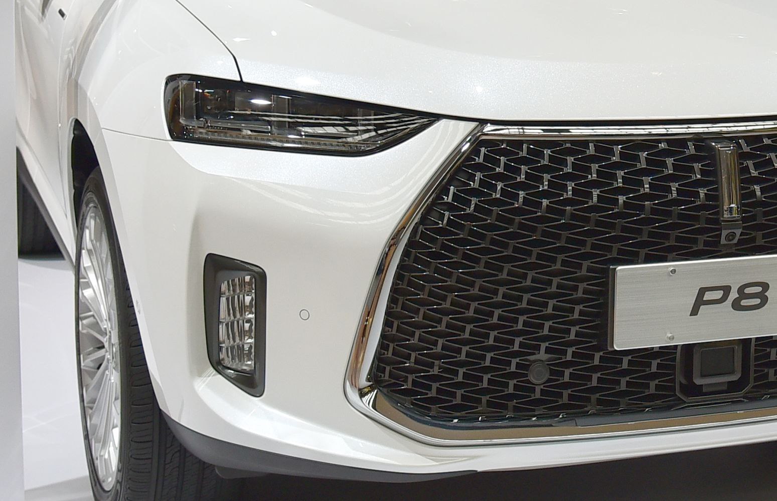 Close-up of front grille and sleek headlight on white vehicle