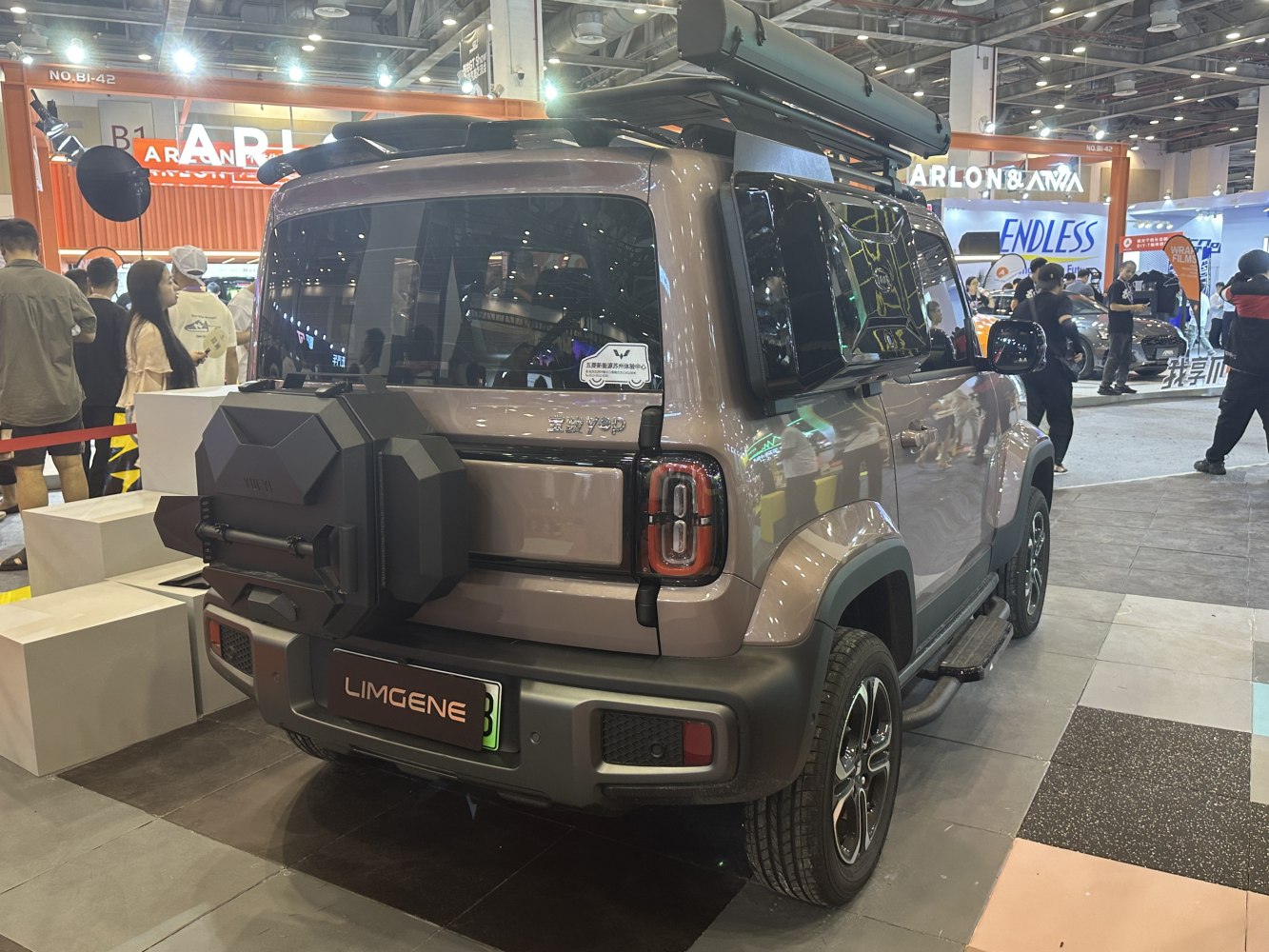 SUV rear view with spare tire mount and roof rack at an indoor auto show.
