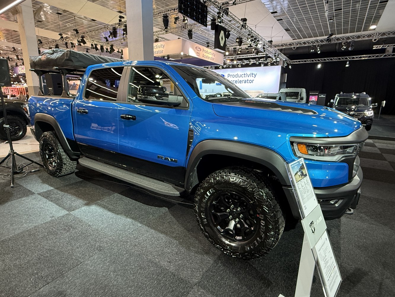 Blue pickup truck with rugged off-road tires and roof rack.