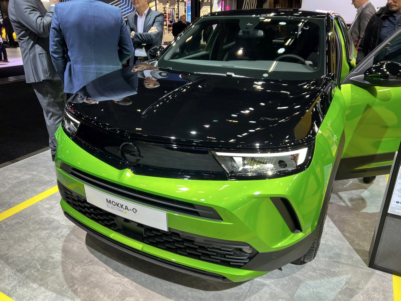 Front view of an electric car with green body and black hood, highlighting modern headlights