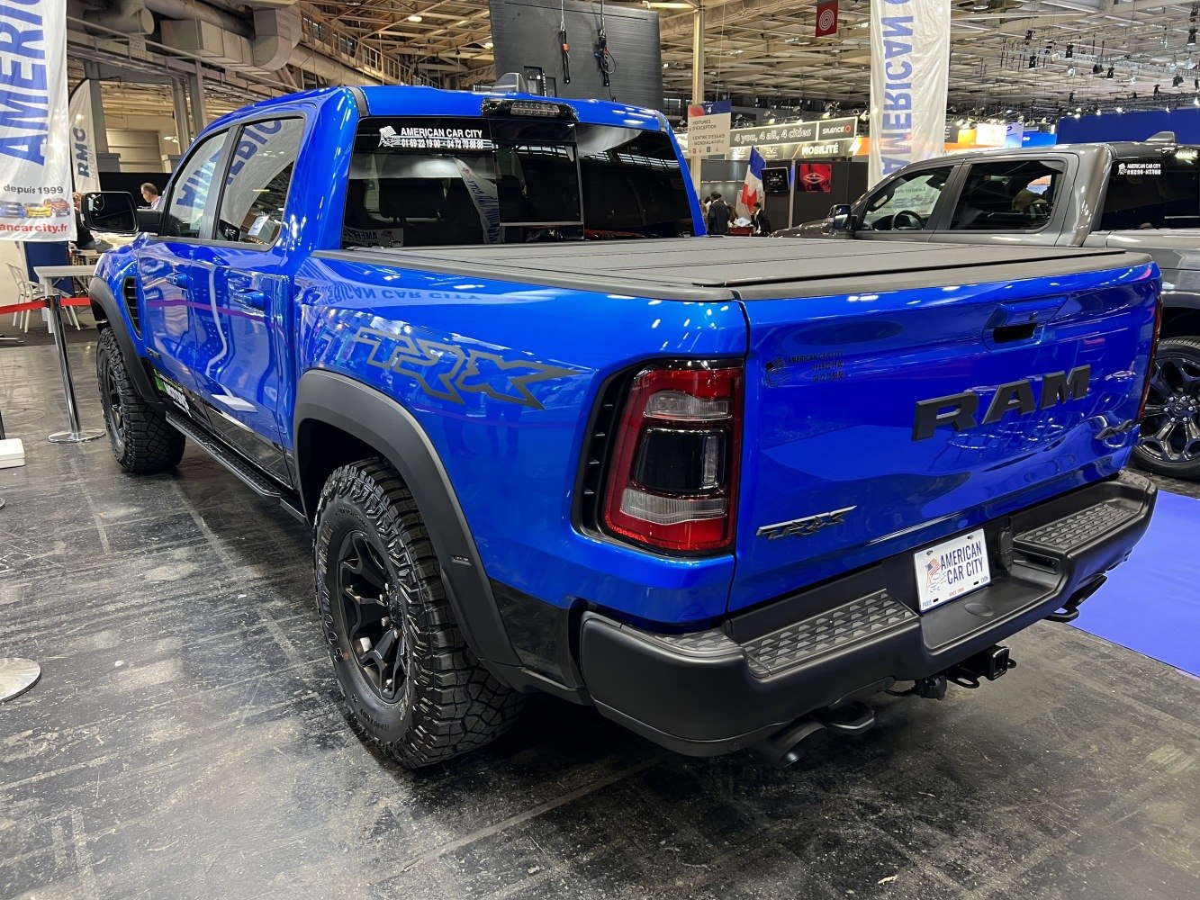 Blue pickup truck rear-side view with off-road tires and bed cover