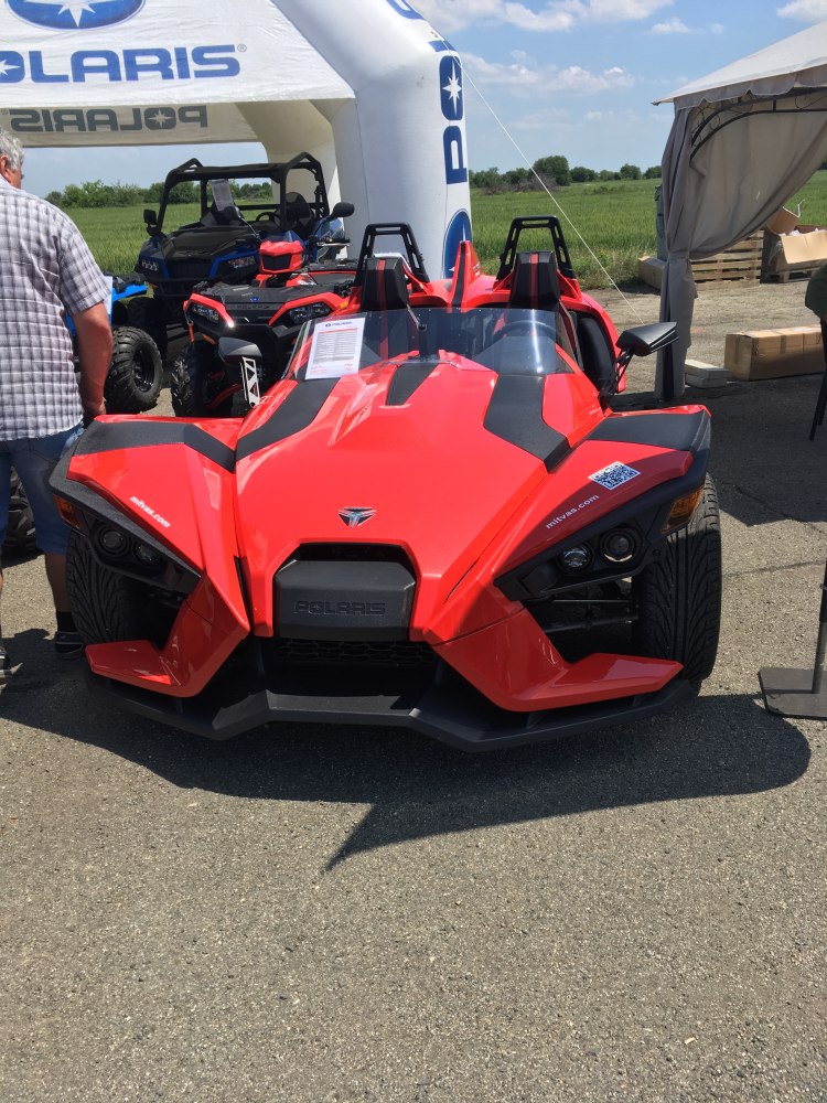 Red three-wheel open cockpit vehicle with angular sporty front design.