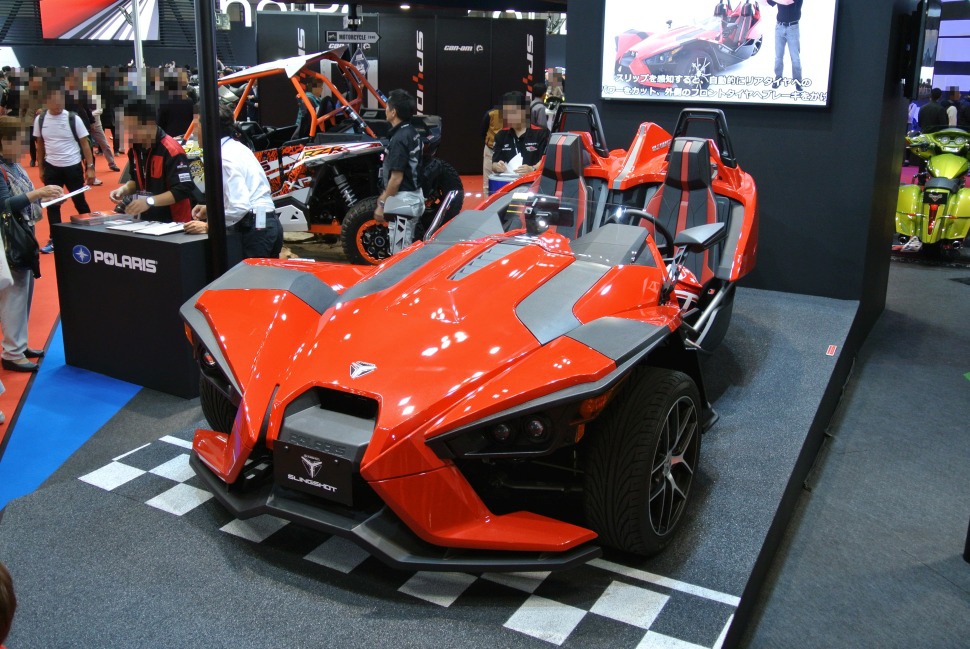Red three-wheeled open-air roadster with angular design and side-by-side seats