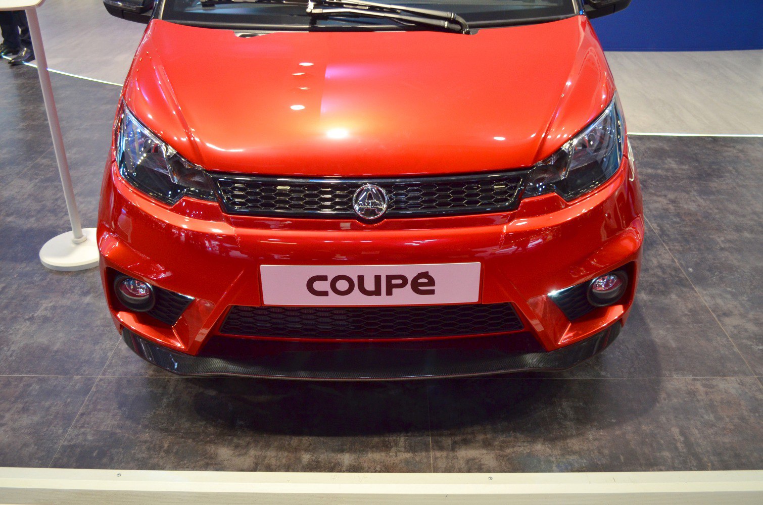 Red compact coupe front with black grille and fog lights