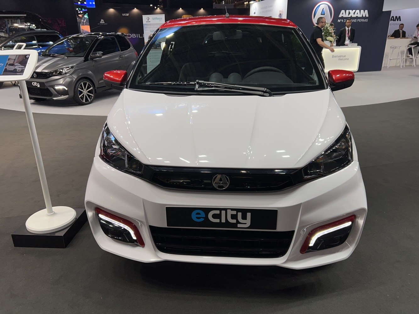 Front view of compact electric microcar with LED daytime running lights and red roof accents