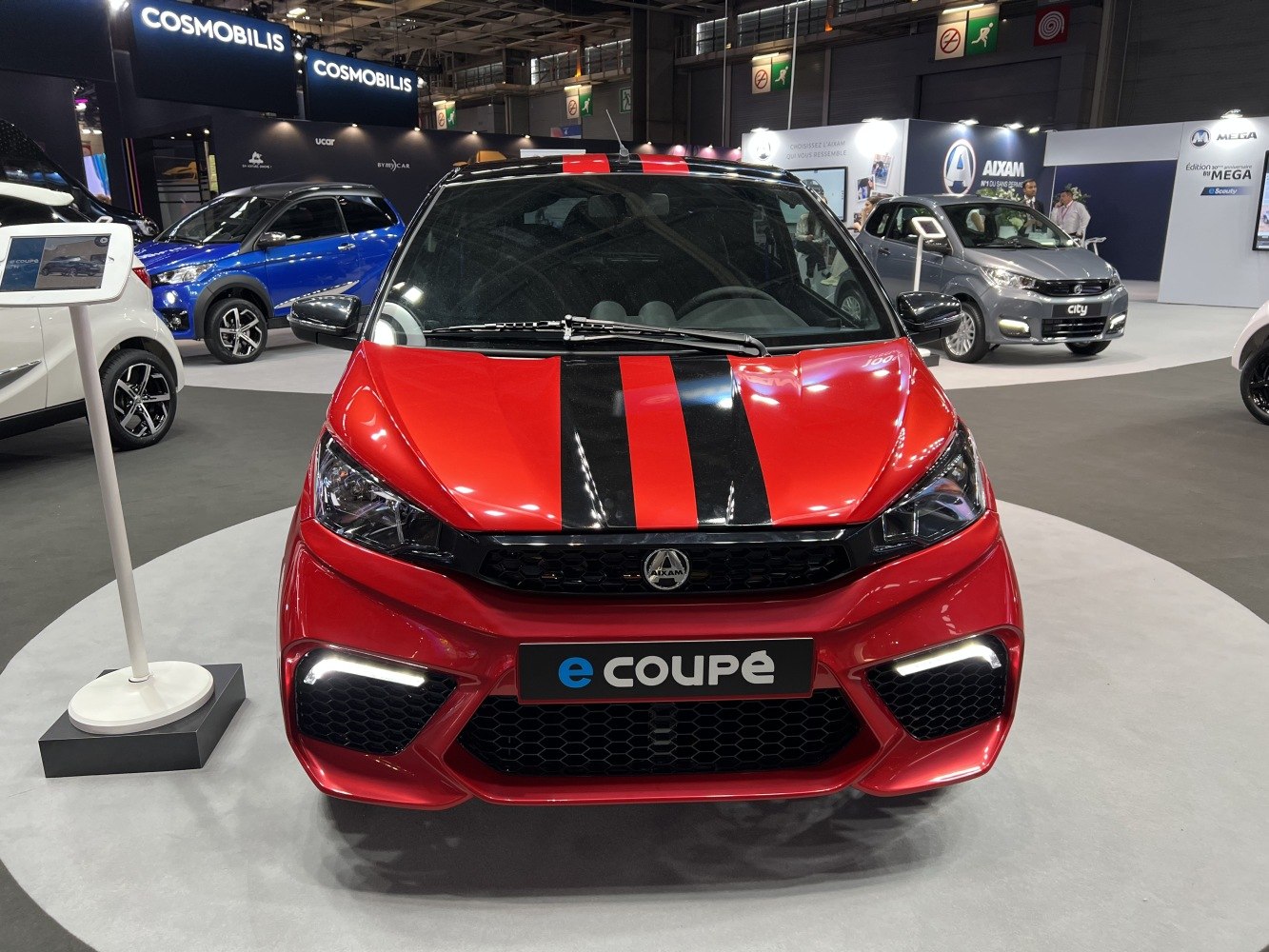 Front view of red compact electric coupe with black racing stripes and LED lights