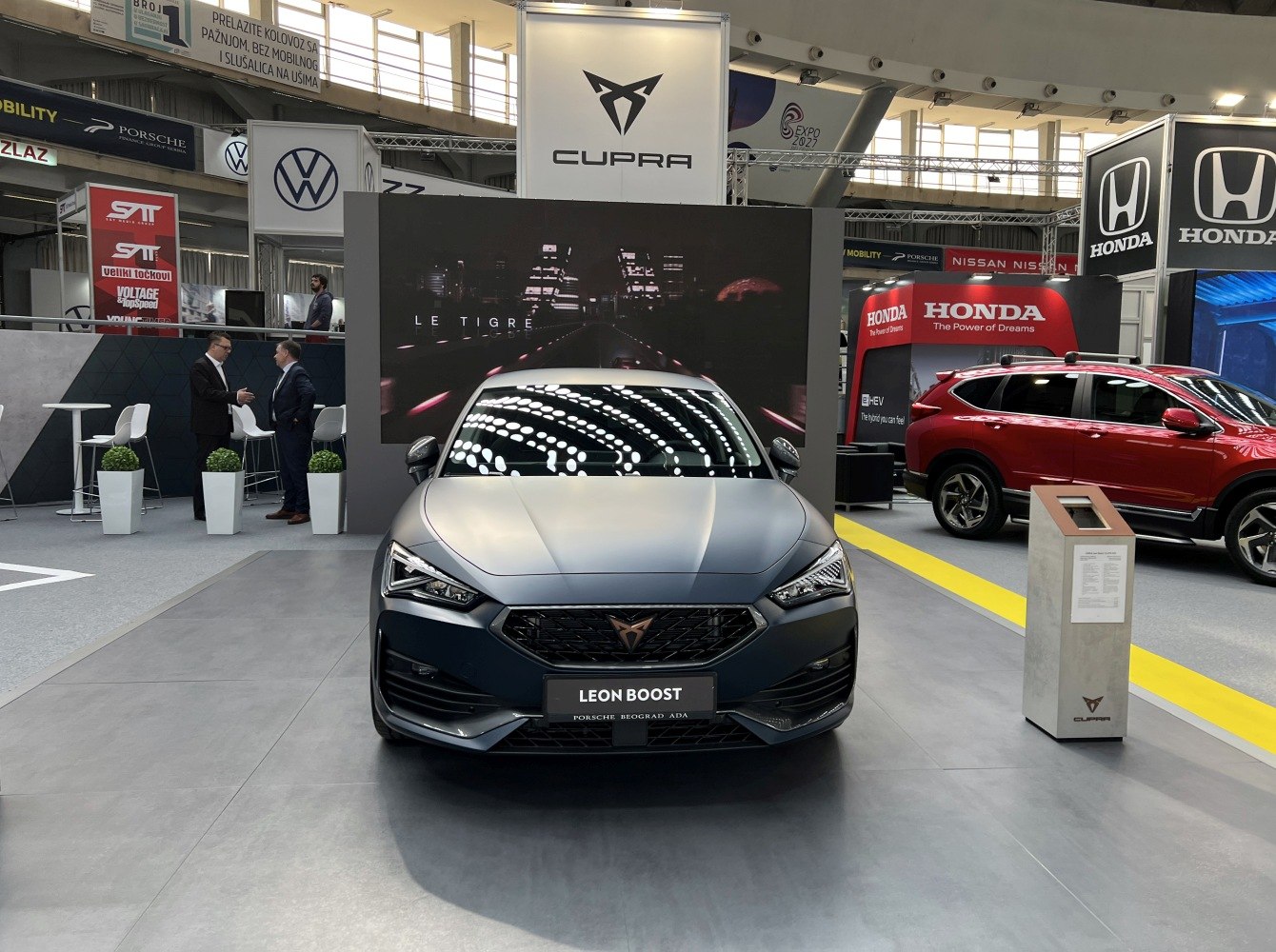 Front view of a sporty matte finish vehicle with sharp headlights and bold grille in an auto exhibition.