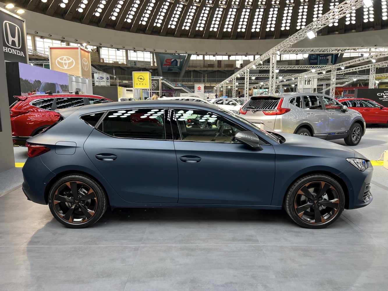 Matte blue hatchback with black and bronze alloy wheels in side view