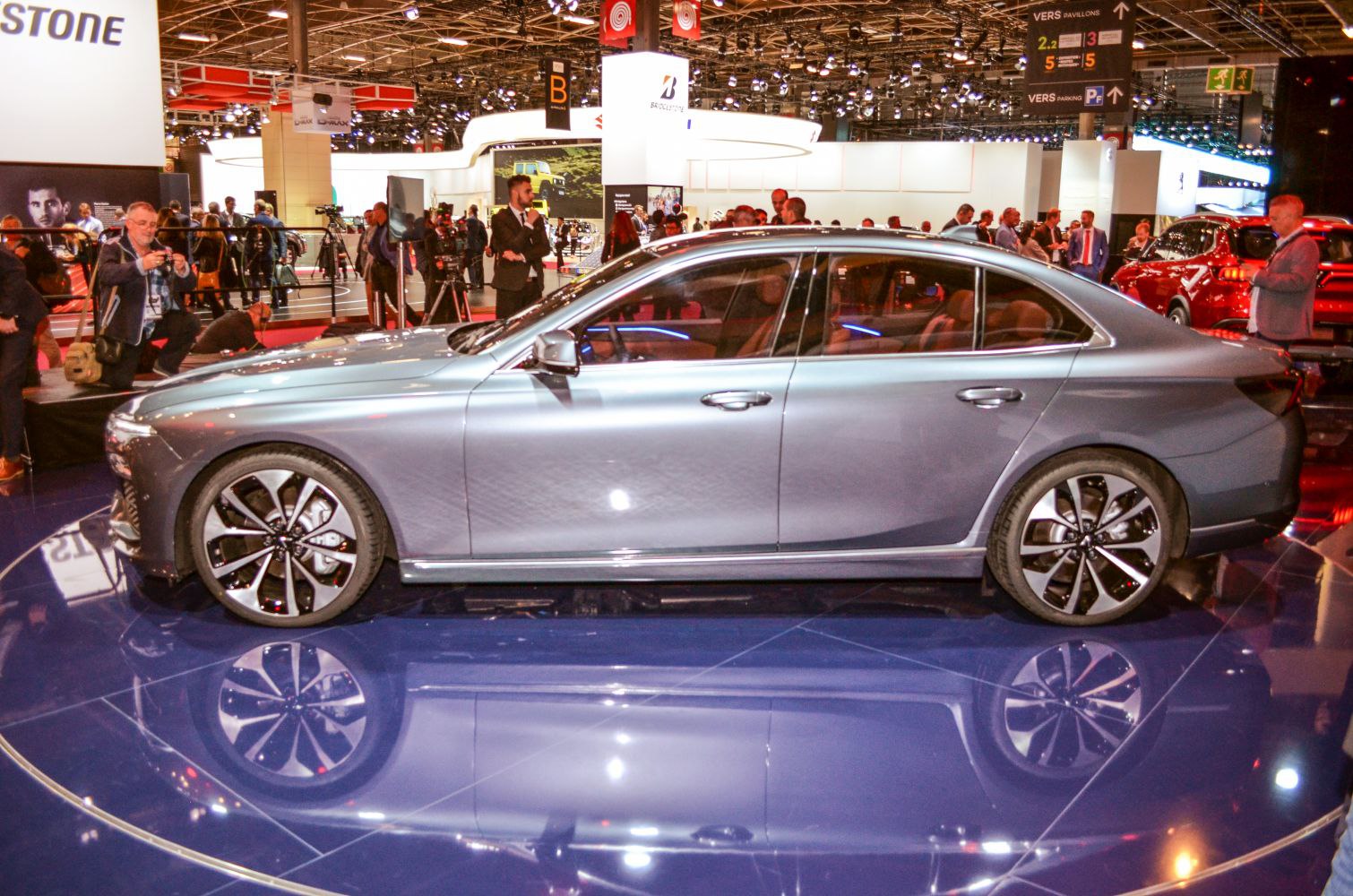 Side profile of a sleek modern sedan with large stylish alloy wheels on reflective floor