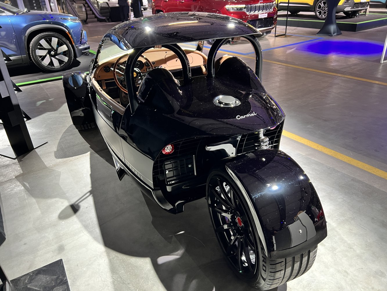 Rear view of a sleek three-wheeled roadster with single rear wheel and open cockpit.