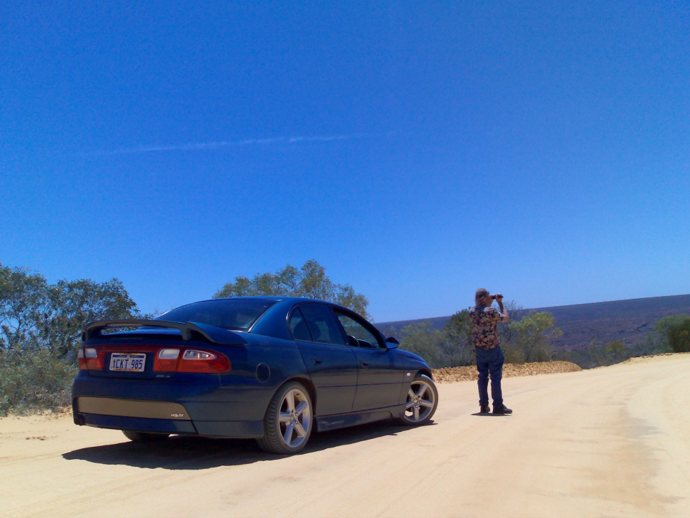 Rear view of a sedan with rear spoiler on a dirt road under blue sky