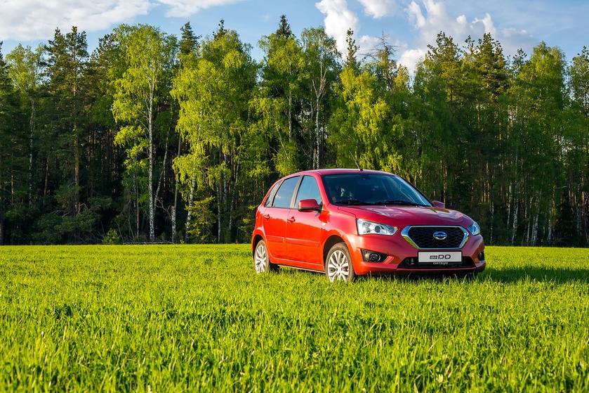 Red hatchback car parked on green grass near forest