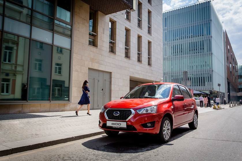 Red hatchback parked on urban street with modern buildings