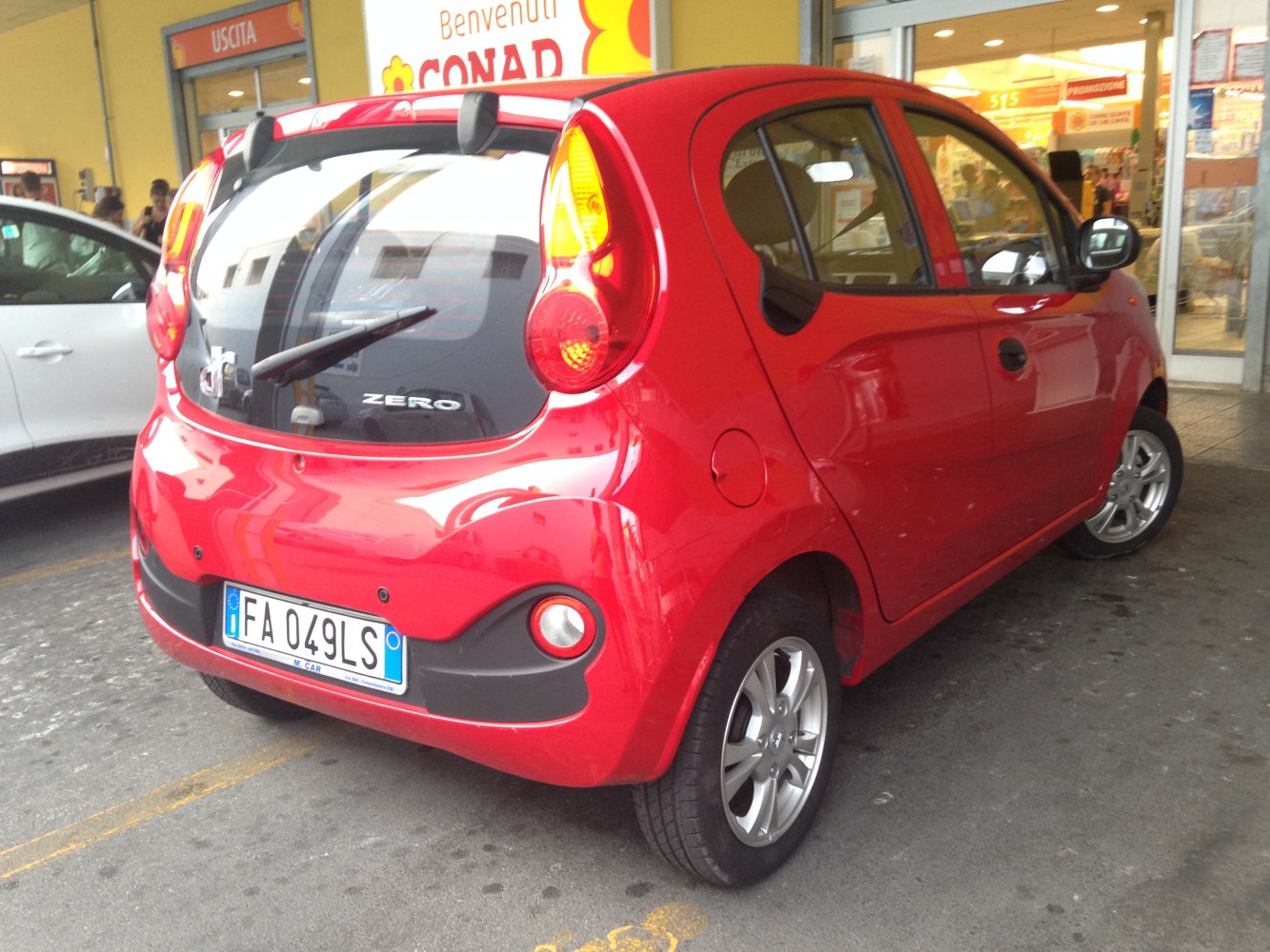 Red compact electric city car rear-side view with distinct tail lights and black bumper.