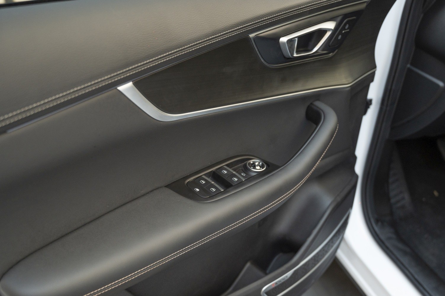 Interior door panel with window controls, handle, and stitched armrest