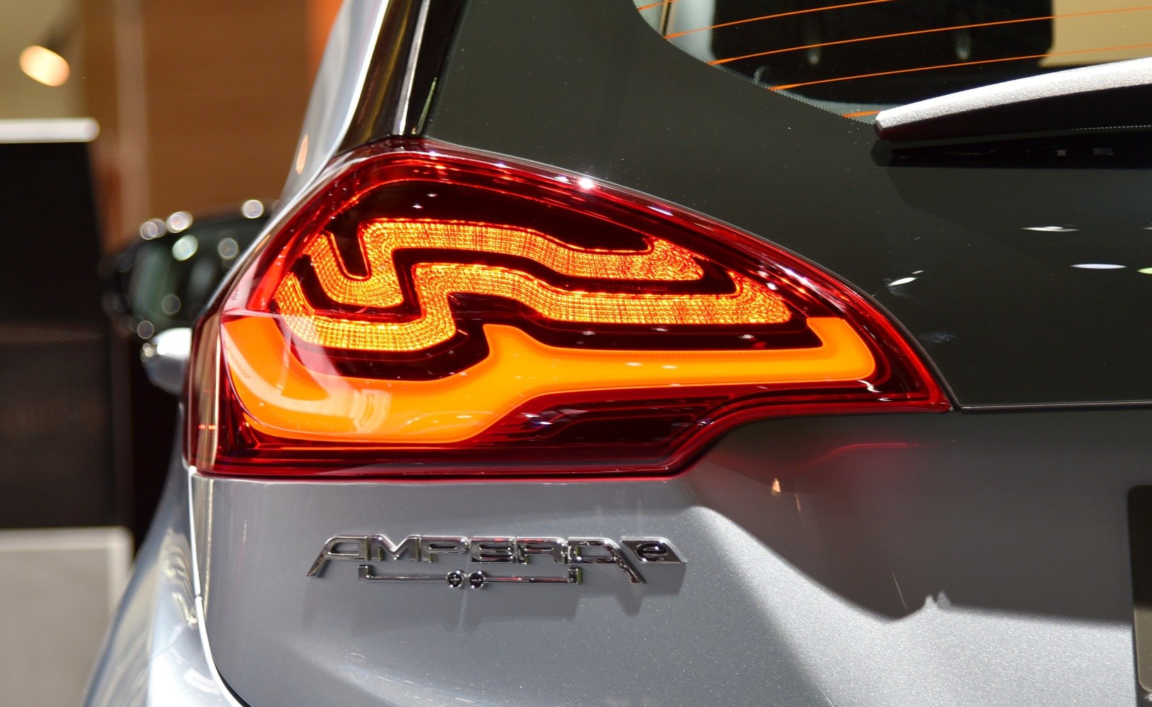 Close-up of illuminated rear taillight and Ampera-e badge on silver car.