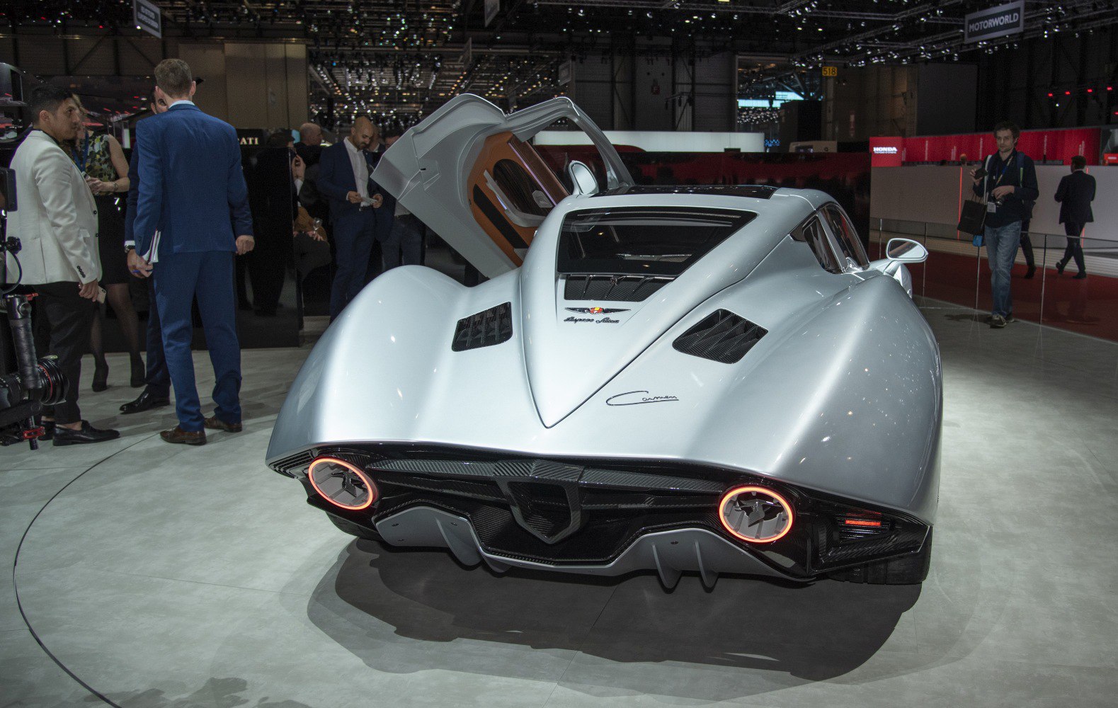 Rear of sleek silver sports coupe with round illuminated taillights and gull-wing door open