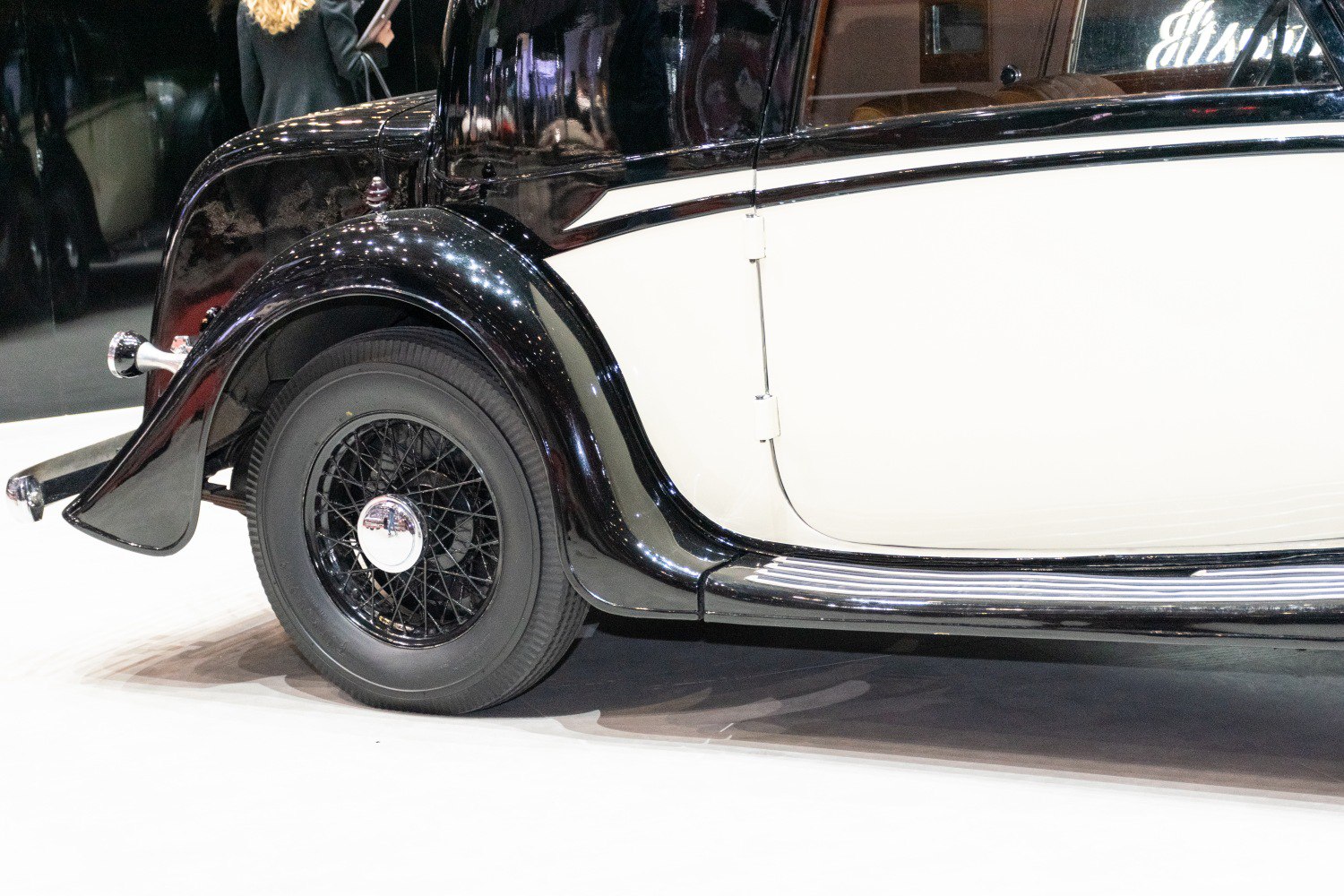 Wire-spoked rear wheel and curved rear fender of black and white classic coupe