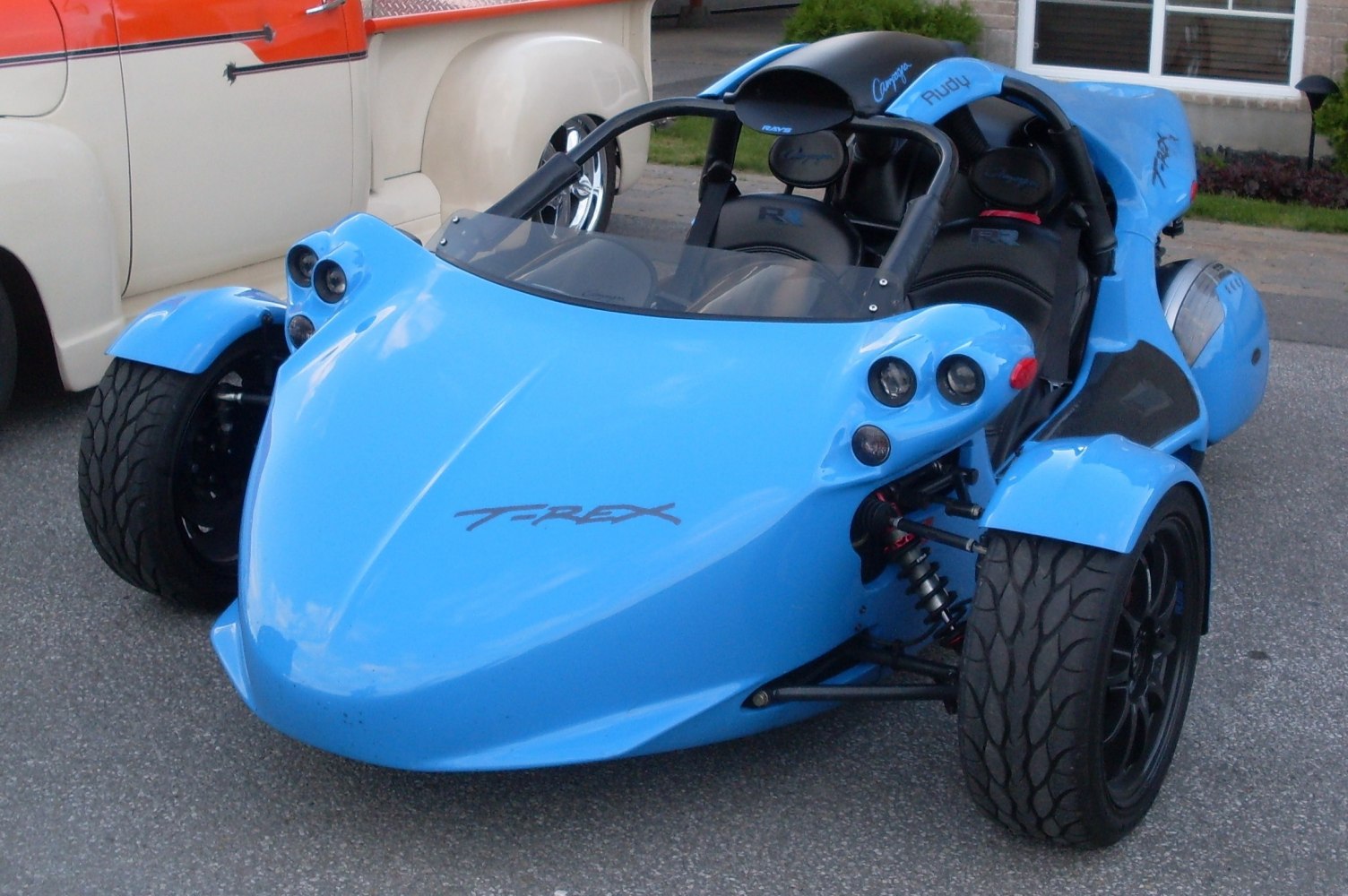 Aerodynamic blue three-wheeled vehicle with dual front tires and open cockpit.