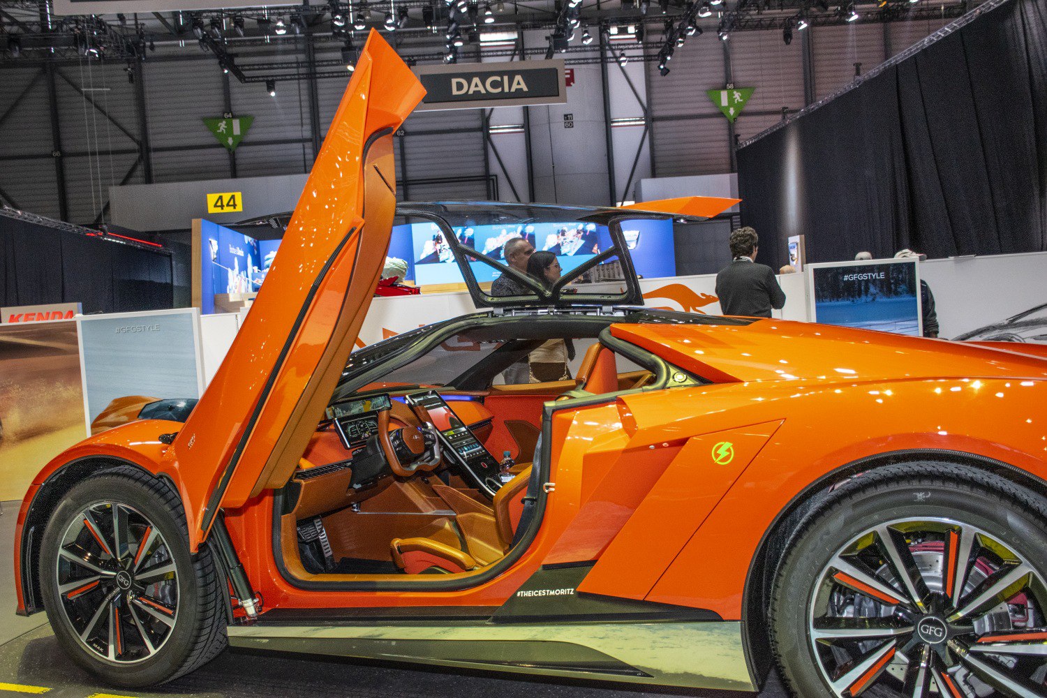Orange sports car with upward-opening scissor doors and visible luxury interior