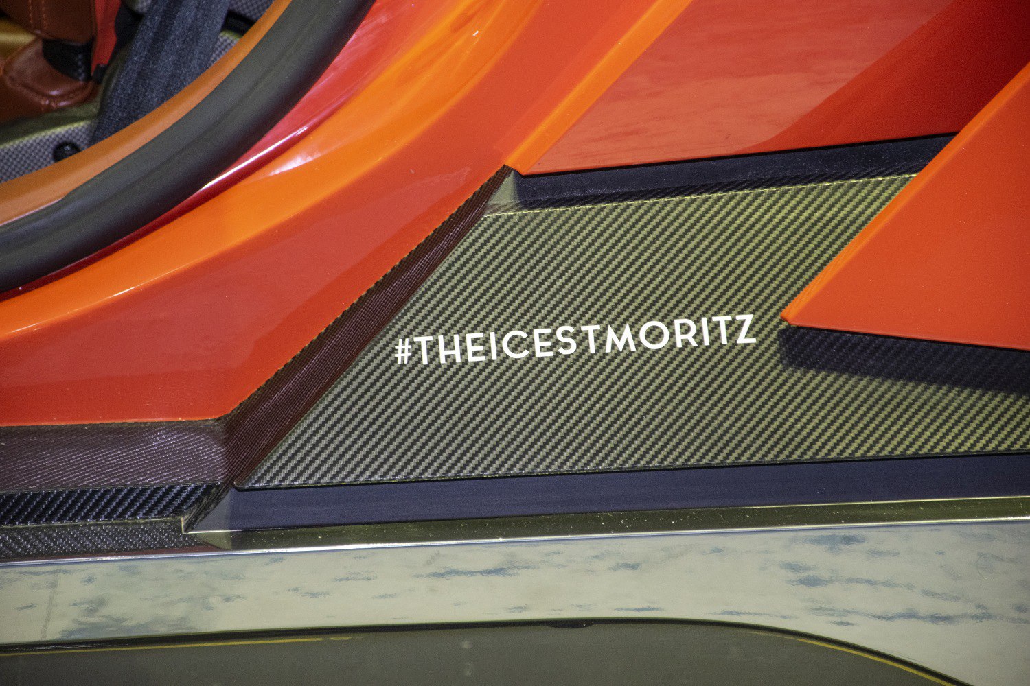 Carbon fiber door sill with #THEICESTMORITZ text and orange car body panel