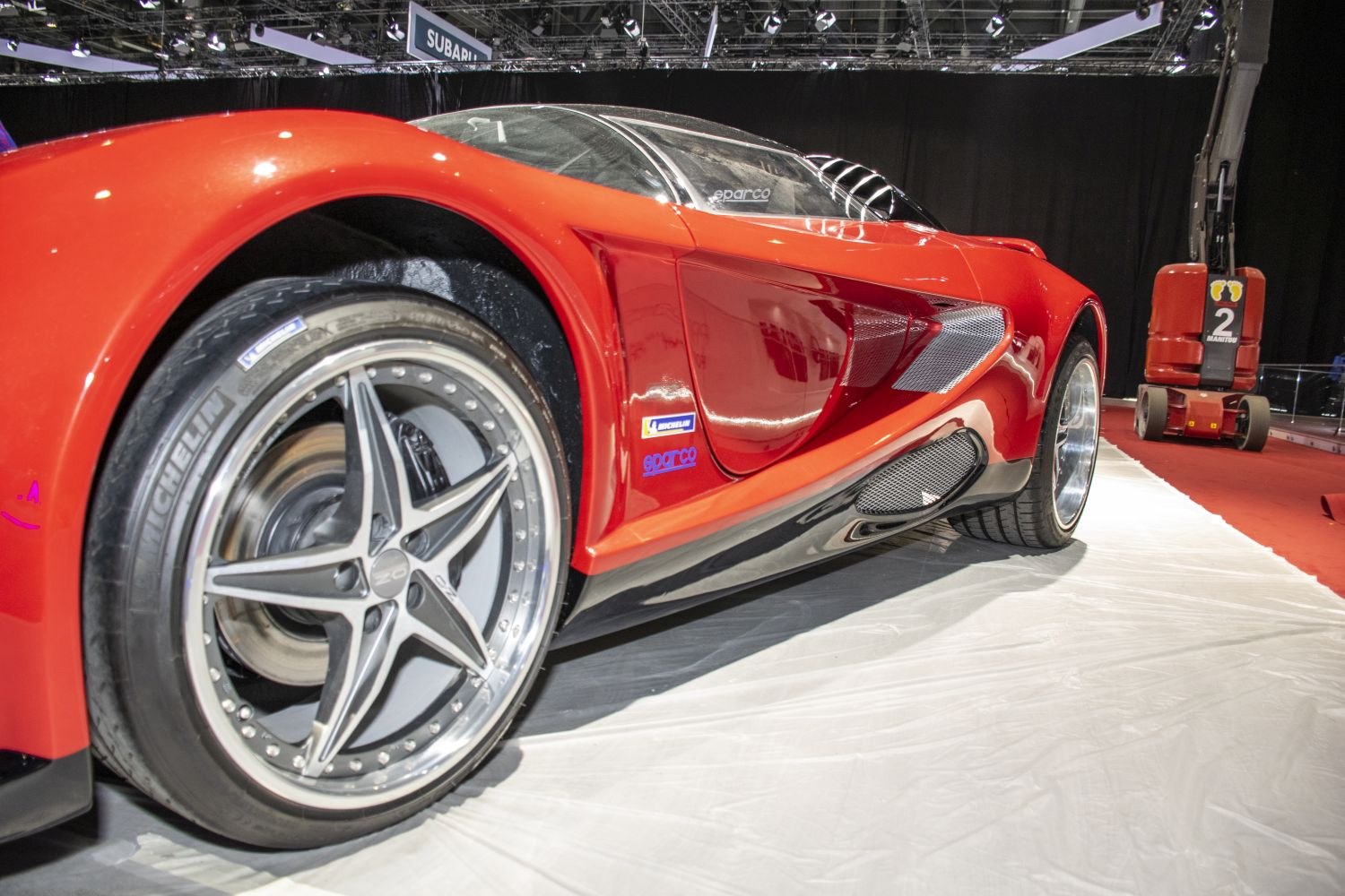 Red sports car side with large air intakes and alloy wheels