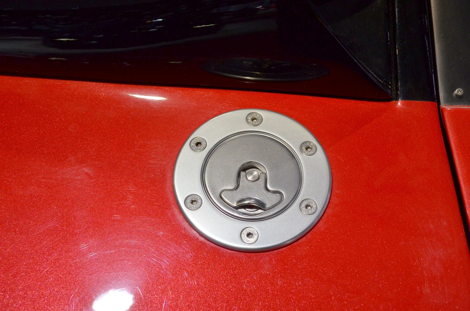 Close-up of circular metal fuel cap with screws on red car body