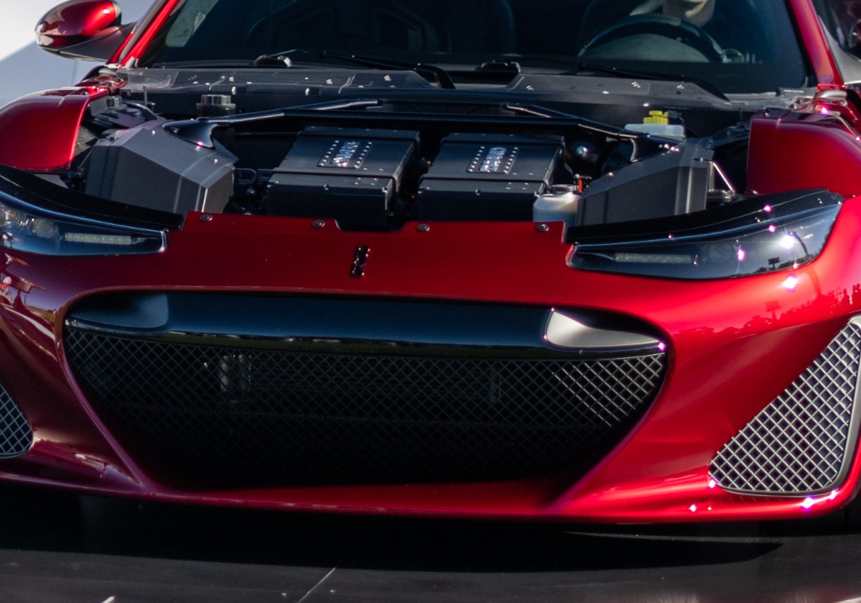 Close-up of car front grille, headlights, and opened hood with engine components