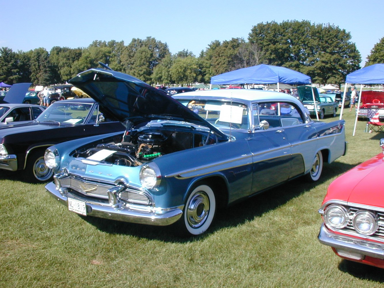 Classic 1950s four-door sedan with open hood showing engine at outdoor car show
