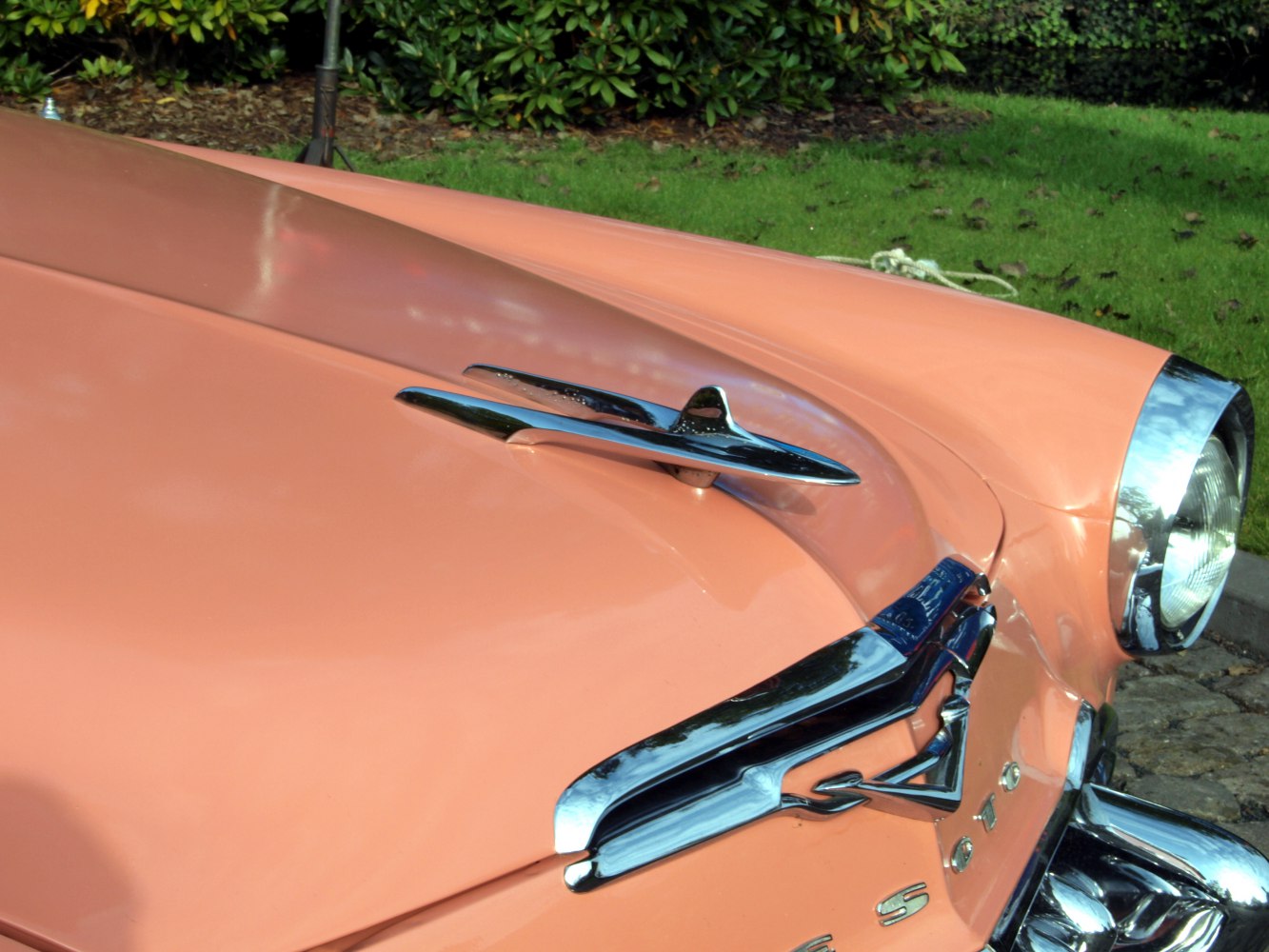 Chrome hood ornament and front trim on peach-colored classic car hood