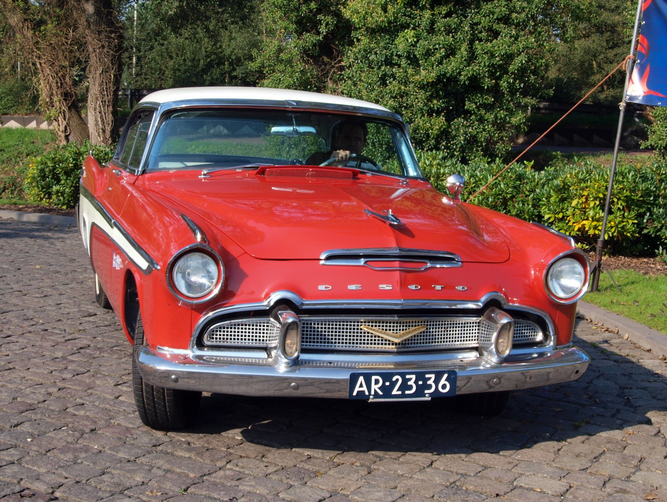 Vintage red two-tone sedan front with round headlights and chrome grille.
