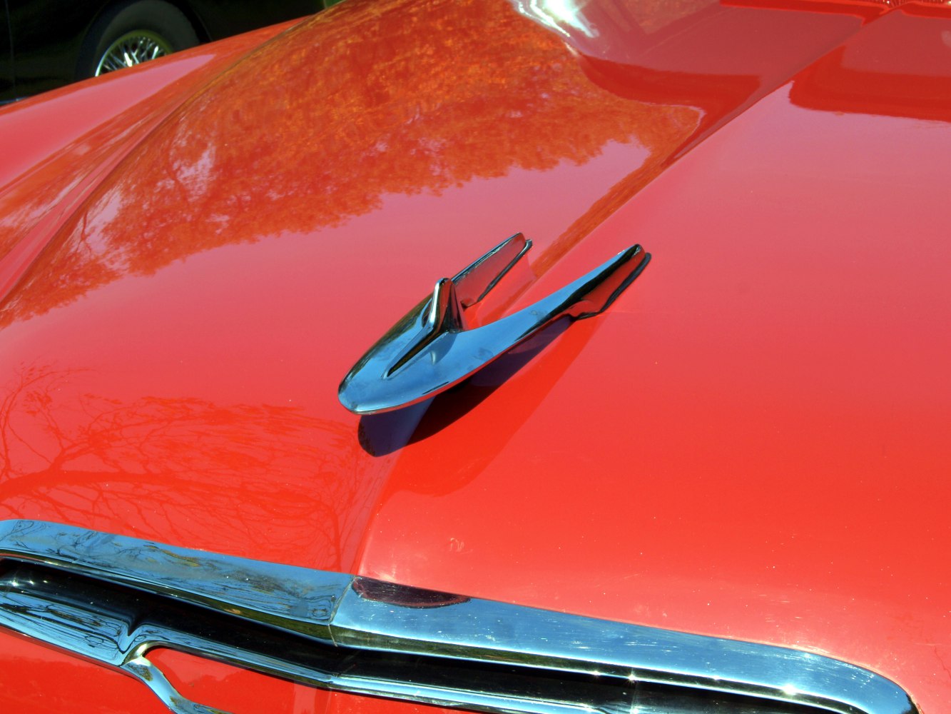 Chrome hood ornament on shiny bright red car hood