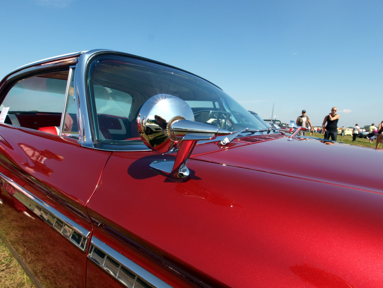 Chrome side mirror and window trim on red vintage car surface