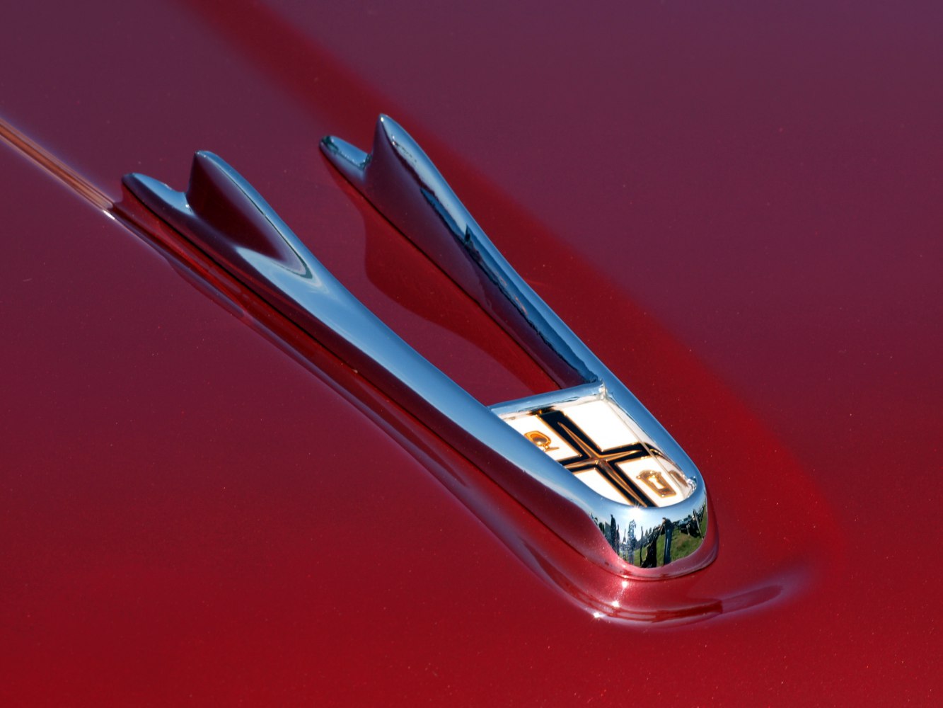 Chrome vintage hood ornament on shiny red surface